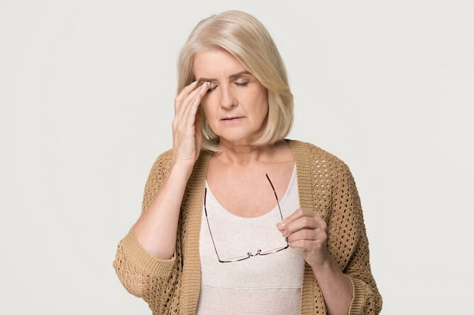 A woman with glasses holds her head, showing signs of discomfort from a headache.