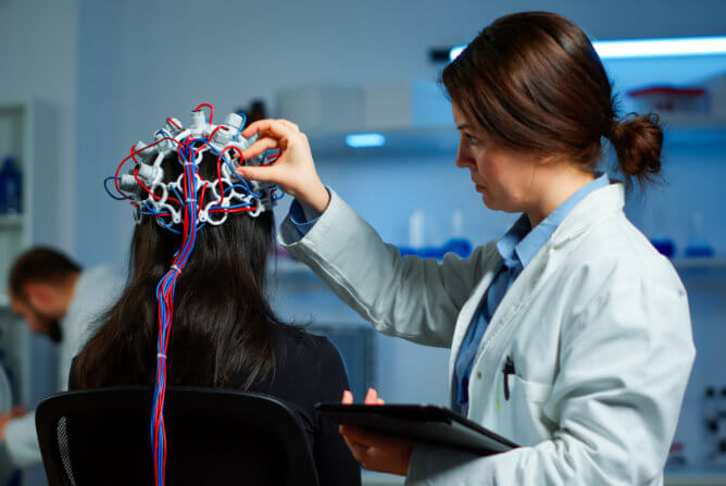 One woman is placing EEG headset on another woman's head, possibly for a diagnostic test or treatment