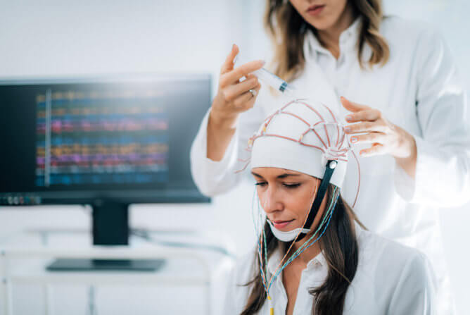 A woman measures a woman's brain activity using an electroencephalogram in a clinical setting.