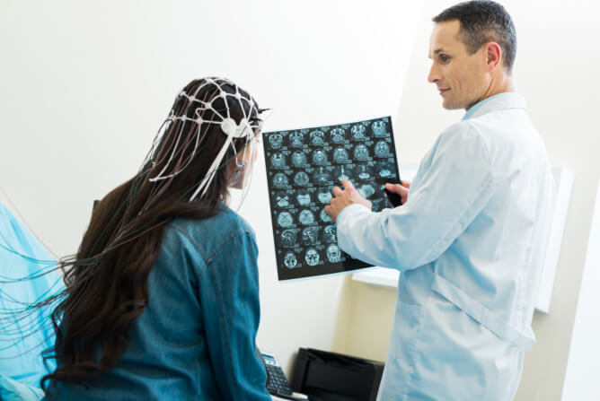 A man and woman are in a medical room with an MRI machine, engaged in conversation about the image results.