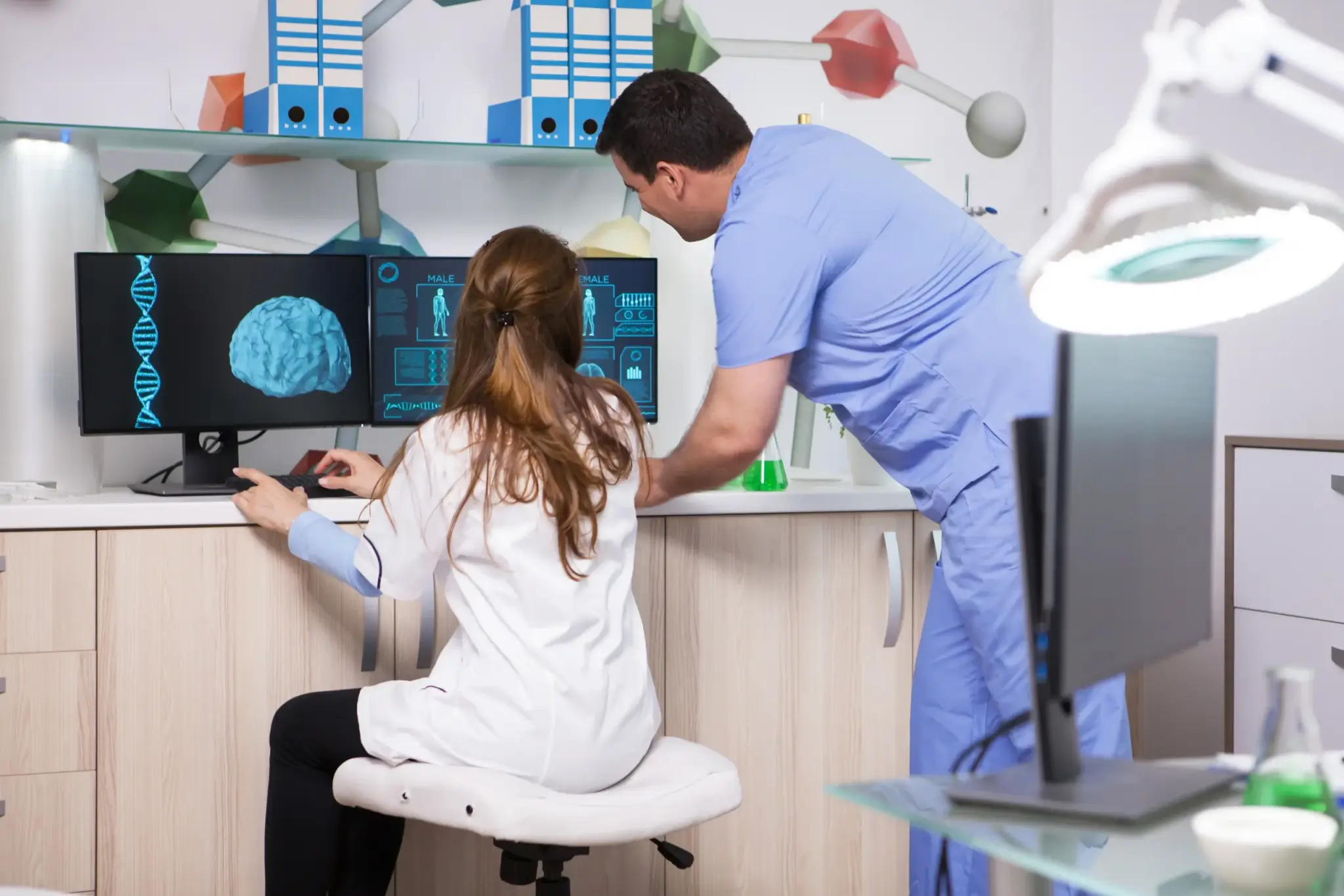 A man and a woman, both medical professionals, reviewing patient information on computer screens